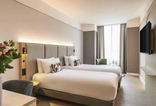 Hotelzimmer mit zwei Einzelbetten, modern eingerichtet, mit großem Fenster.
