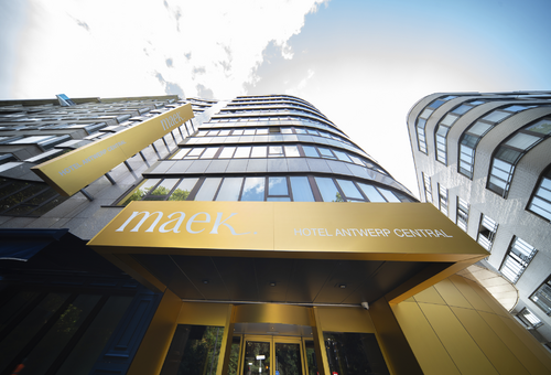 Fassade des MAEK Hotels Antwerp Central mit gelben Schildern und modernen Glasfenstern.
